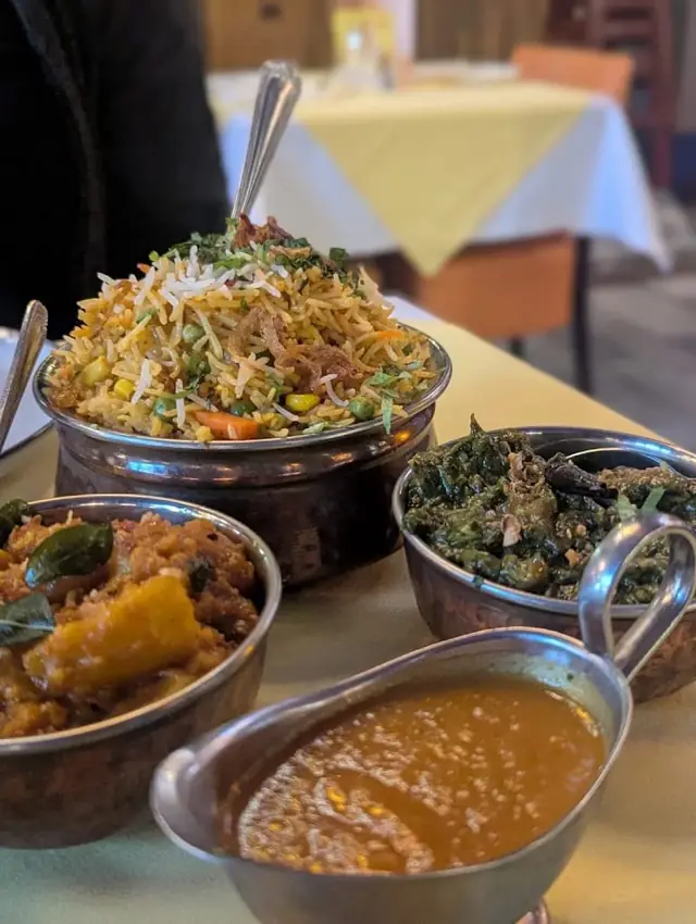 A copper pot of biryani topped with herbs, beside curries and sauce