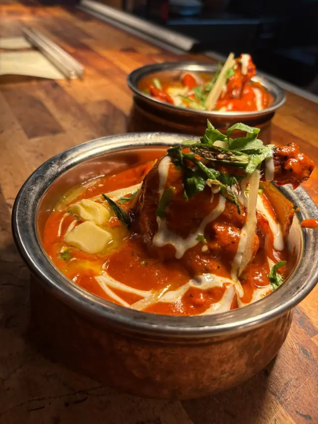 A rich lamb curry in a copper handi garnished with ginger and coriander