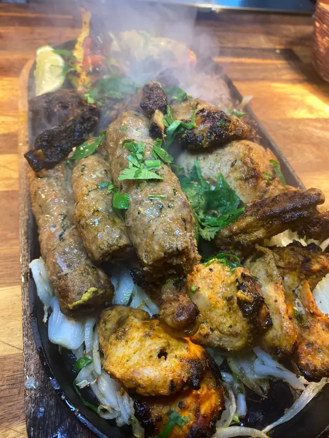 A long sizzler platter of kebabs and tikka steaming on the table