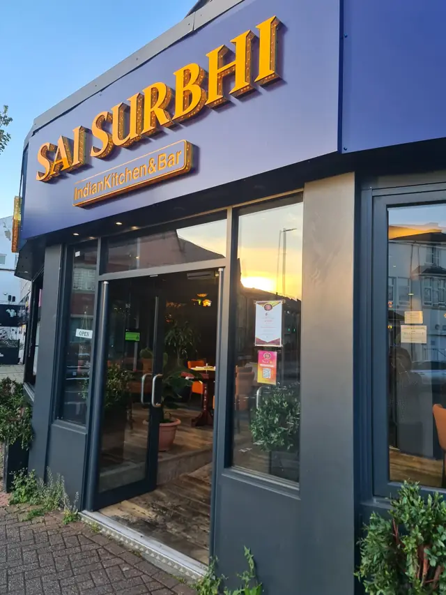The Sai Surbhi shopfront on Station Road at sunset, with the blue and gold Indian Kitchen & Bar sign